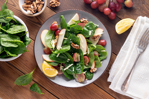 Healthy spinach salad made with red apple, wallnuts, grapes. Wooden rustic background