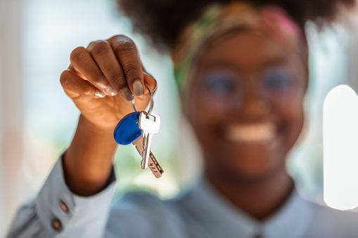 Close up focus on keys in female african ethnicity hands, joyful sincere mixed race blurred woman feeling excited of buying own house apartment.