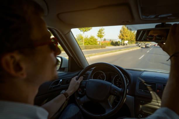istock While driving the car, young Caucasian man adjusting the rear-view mirror 1350882524