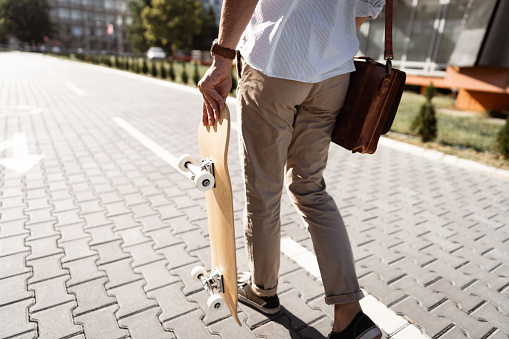 Modern unrecognizable Caucasian man, holding a skateboard, while commuting to the work or Univeristy