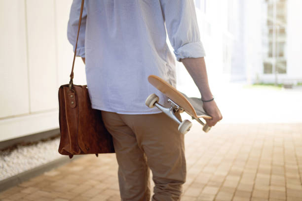 istock Rear-view of an unrecognizable Caucasian man holding a skateboard, while commuting to work 1350883924