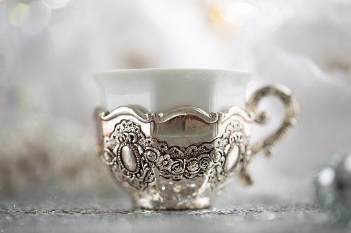 Vintage coffee silver cup and blurred light background. Soft focus. Shallow depth of field. Antique white porcelain. Festive Christmas table setting with a cup.