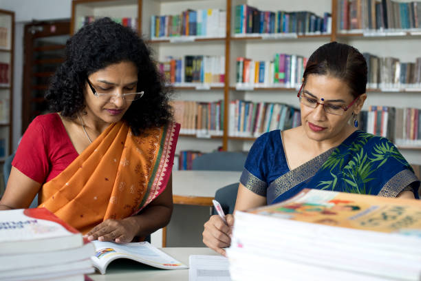 istock Two teachers writing and reading books in library 1350887329