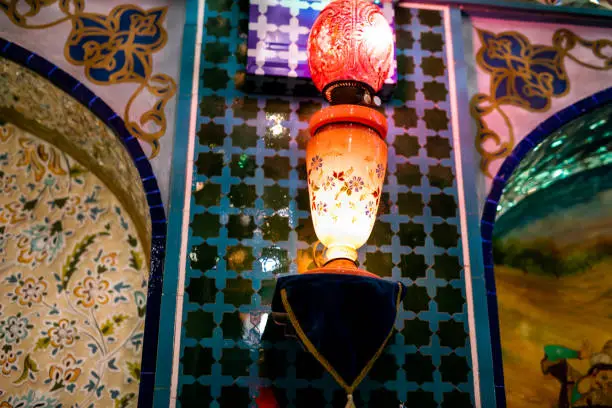 Photo of Glow in the dark lantern. Lighted old fashioned lantern background. An outdated light concept with a soft shadow. Red and yellow fire. An old-fashioned lantern illuminated by a hurricane in the dark. The concept of lighting, lighting and new life.