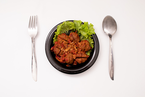 Homemade meatballs with tomato sauce and spices served on a black plate on a white background