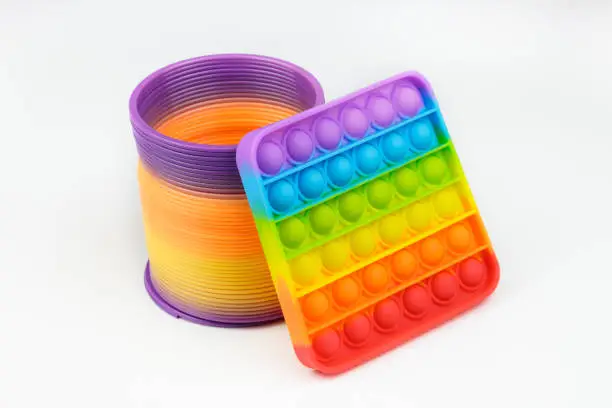 Photo of Popular plastic Slinky toy and Rainbow Square Fidget Toys Pop-it on the white background