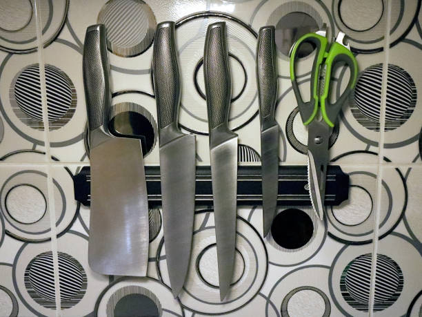 A set of knives and kitchen scissors on a magnetic holder.