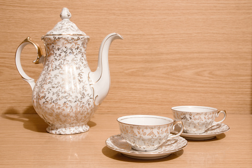 Tea set with golden ornaments, two small teacups with plates and teapot on a wooden background