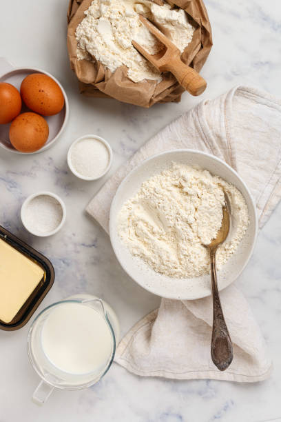 istock white plate with wheat flour and ingredients for making dough - eggs, milk, salt, sugar, butter on a marble background. The concept of home baking. Selective focus, top view 1350903316