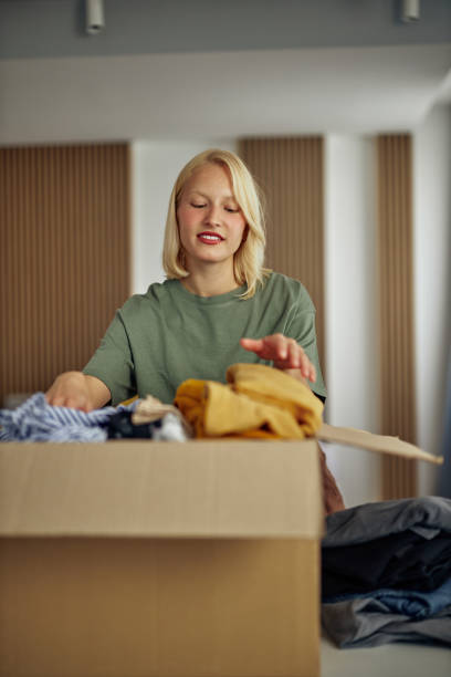 istock Woman folding and packing used clothes into cardboard donation box. 1350906360