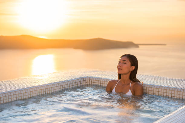 spa hotel di lusso relax jacuzzi terapia piscina donna asiatica che si rilassa nella vasca idromassaggio del resort all'esterno sulla camera privata balcone tramonto sul mare. europa luna di miele vacanza relax benessere coccole. - santorini greece villa beach foto e immagini stock