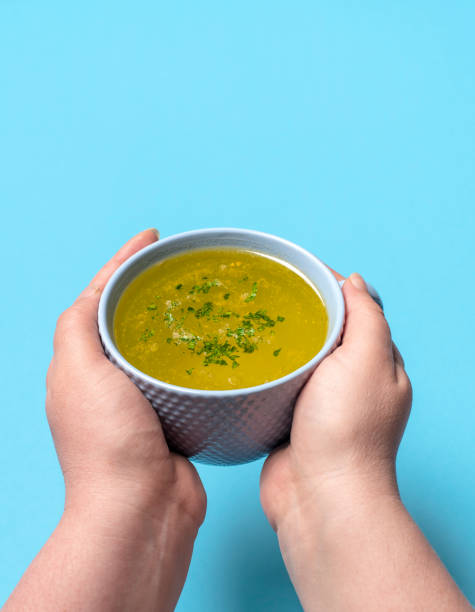 istock Chicken soup mug in woman hands on a blue background. 1350907762