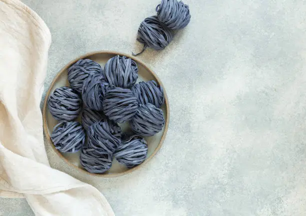 Photo of Raw organic wheat blue noodles with anchana flowers. The concept of a healthy and sporty lifestyle. butterfly pea flowers.  Thai cuisine. Selective focus, Top view and Copy Space