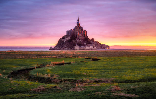 Sunrise at Mont Saint Michelle View of Le Mont Saint Michel at sunrise with low tide and pink colors from the meanders. Normandy, France grassland in morning sunrise stock pictures, royalty-free photos & images
