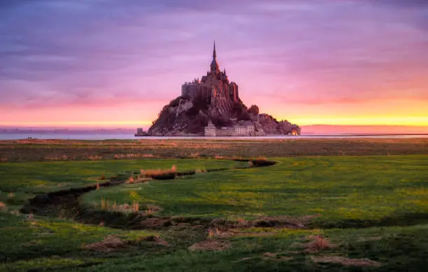 View of Le Mont Saint Michel at sunrise with low tide and pink colors from the meanders. Normandy, France