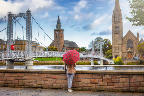 un turista con un paraguas de patrón escocés disfruta de la vista al paisaje urbano de inverness - inverness area fotografías e imágenes de stock