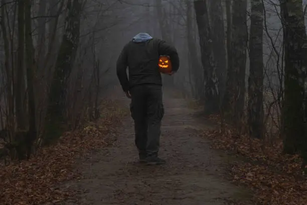 Photo of Headless man with Halloween pumpkin in foggy forest