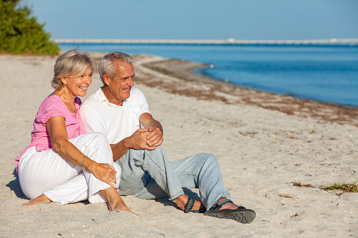 Happy senior man and woman couple sitting, smiling and laughing on a sunny beach