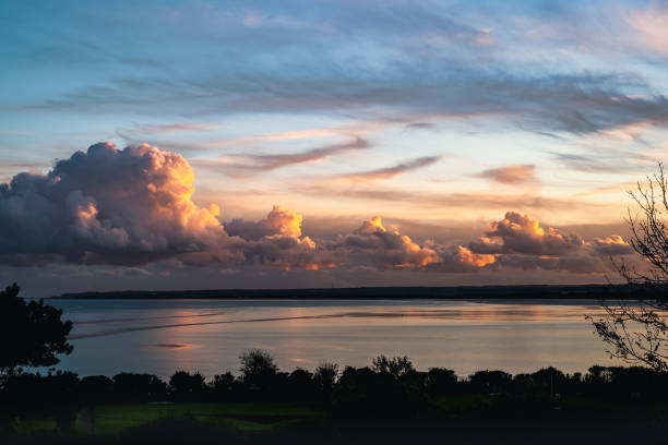 impressive billowing cumulus clouds at dusk along the horizon and reflecting in the sea. The clouds are highlighted by the gold, red glow of the sunset. impressive billowing cumulus clouds at dusk along the horizon and reflecting in the sea. The clouds are highlighted by the gold, red glow of the sunset. sandwich kent stock pictures, royalty-free photos & images
