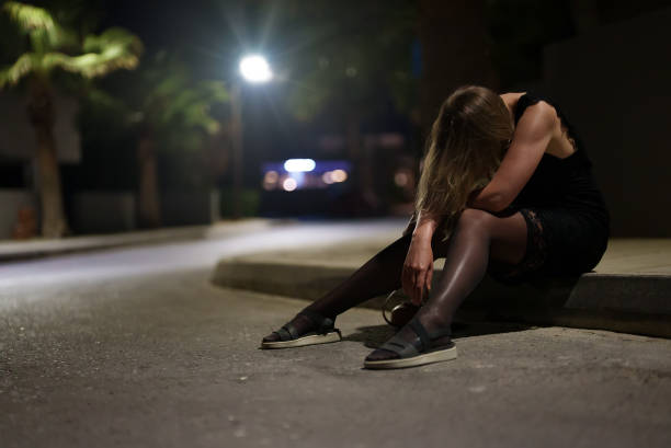 Drunk woman in dress sits on the roadside at night. stock photo