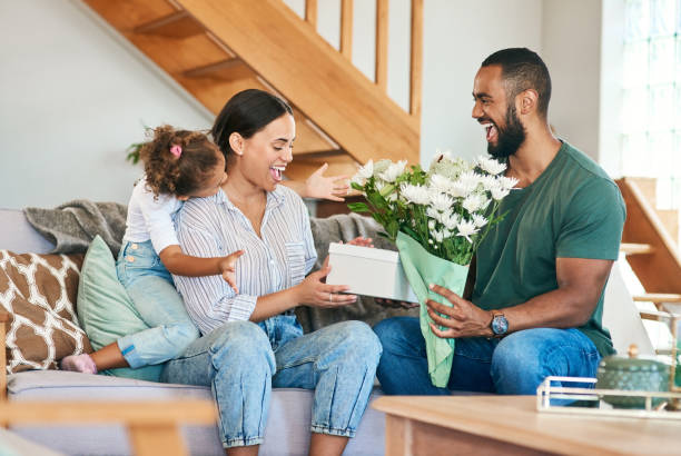 tiro de uma mulher recebendo um presente e buquê de flores de seu marido e filha pequena em casa - family loving anniversary gift - fotografias e filmes do acervo