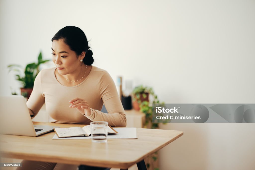 Happy Business Woman Working from Home on Laptop Computer Beautiful Asian businesswoman using laptop computer while sitting at desk in a living room Writing - Activity Stock Photo