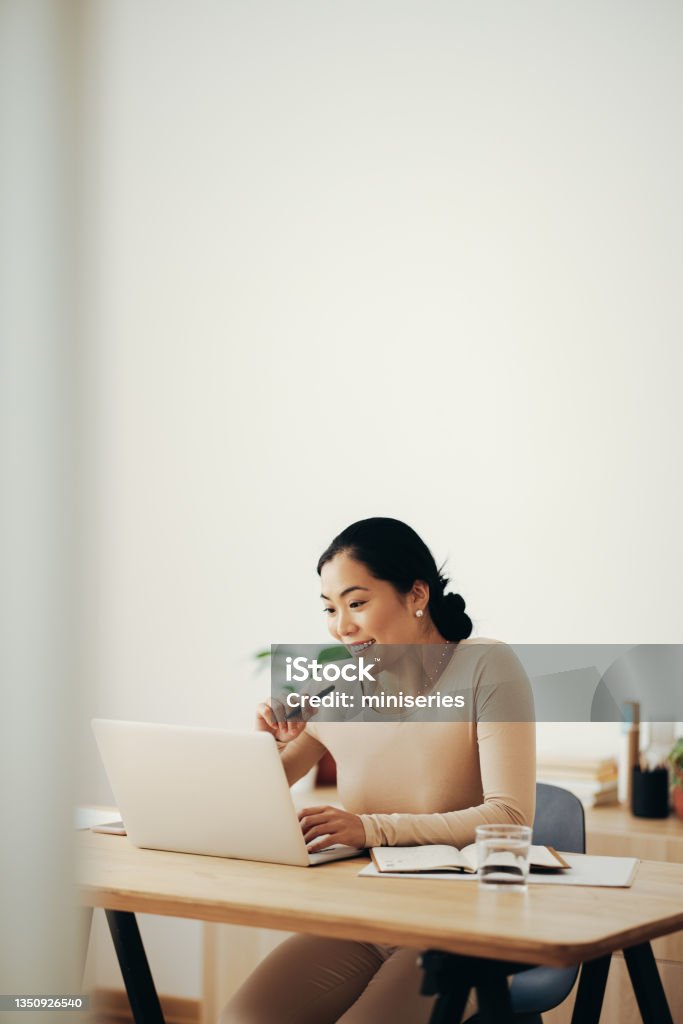 Happy Business Woman Working from Home on Laptop Computer Beautiful smiling Asian businesswoman reading business report on a laptop computer while sitting at desk in a living room People Stock Photo