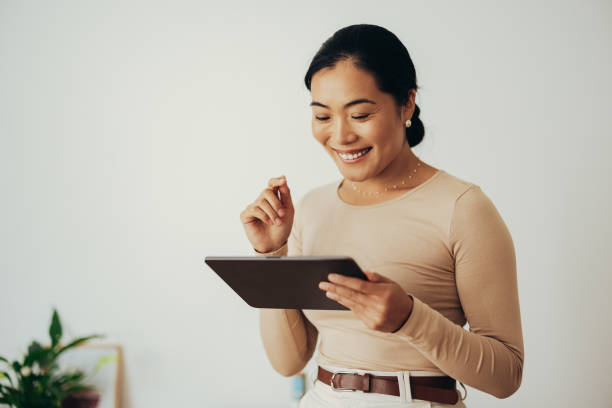 femme d’affaires heureuse utilisant une tablette numérique à la maison - using tablet photos et images de collection