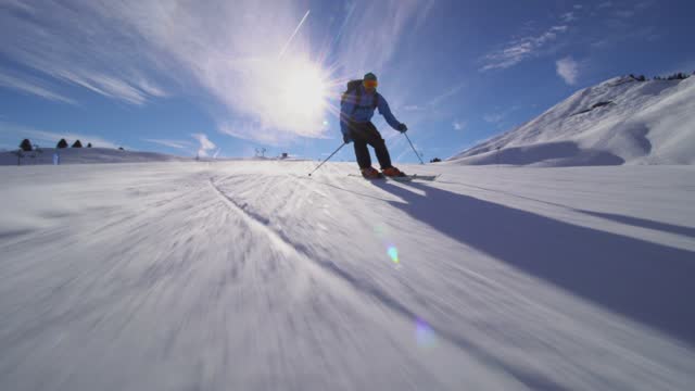 Professional skier skiing on slopes in the Swiss alps. Sun rays and lens flare visible.