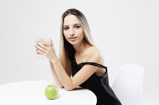 health and people concept - young woman wearing pajamas holding water glass