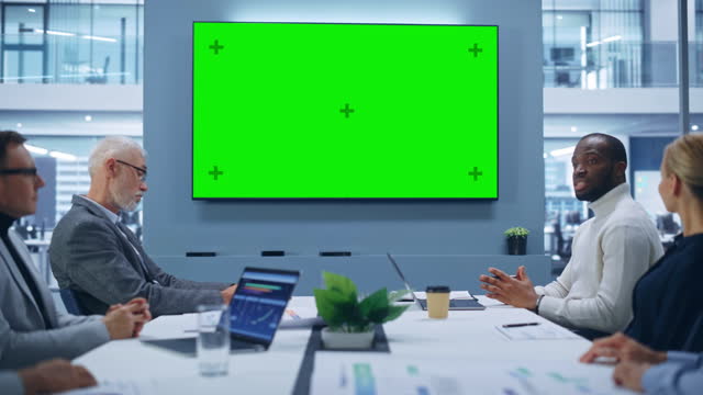 Multi-Ethnic Office Conference Room Meeting: Diverse Team of Successful Managers, Executives Talk, Use Green Screen Chroma Key TV. Group of Businesspeople Work on Strategy for an e-Commerce Startup