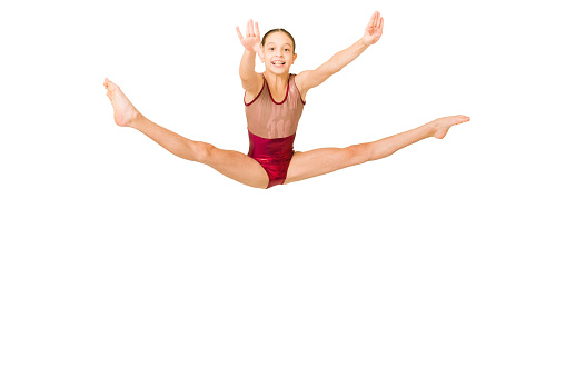 Excited sporty gymnast smiling while jumping and doing a leg split. Cheerful girl performing on a sports competition