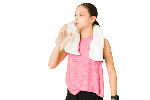 Fit beautiful girl with a towel taking a break from her workout and drinking water. Tired active teen resting from exercise