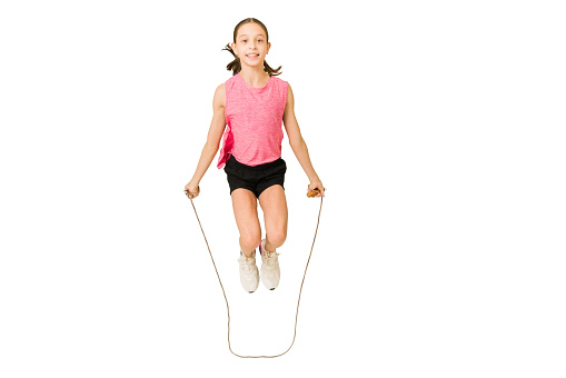 Cheerful young child in sportswear smiling and enjoying jumping the rope against a white background