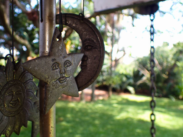 Ornamental home garden wind chime with celestial figures close-up with lush green garden defocused