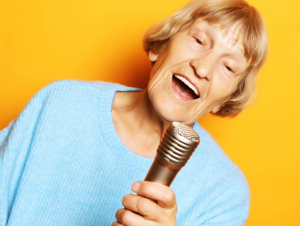 istock Happy old senior woman singing with microphone, having fun, expressing musical talent over yellow background 1350945887