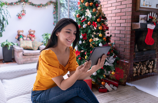 Beautiful woman at home relaxing on couch while watching videos on tablet during christmas season - Lifestyles