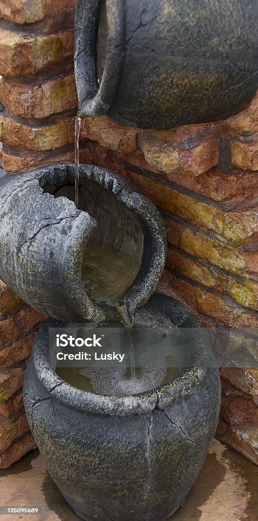 Trickle Down effect Water flowing through a waterfall of cast jugs fixed into a brick wall. Jug Stock Photo