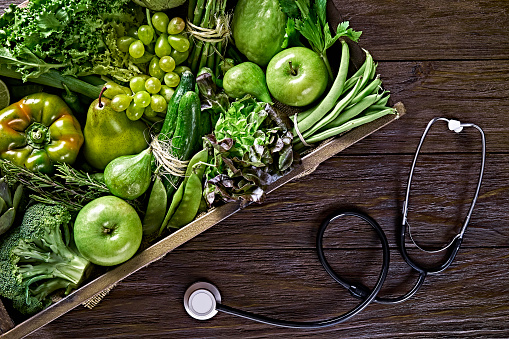 Healthy food and diet concept: Table top view background of a variation green vegetables for detox and alkaline diet with stethoscope. Set in a crate on a wooden rustic table