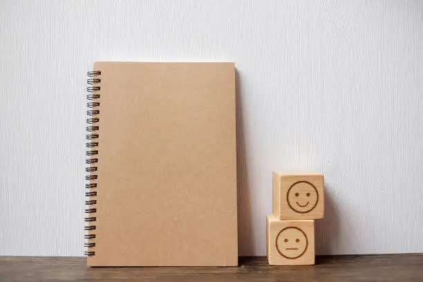 Photo of emotion face block and notebook on table. Emoticon for customer review, satisfaction, mood, mental health and feedback concept