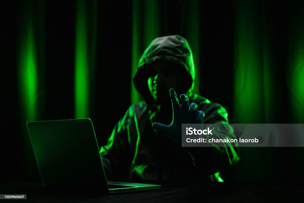 Hackers wear hoods to cover their faces. Hacking to steal important information. Use a computer to release malware viruses Ransom and harass organizations. He sitting in the dark room with neon light Adult Stock Photo