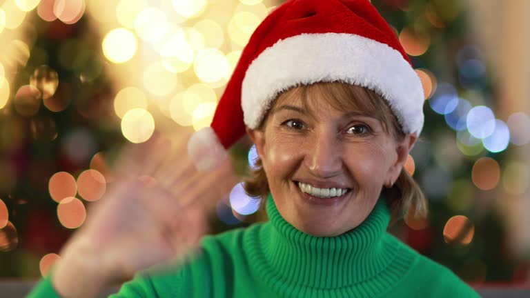 Smiling woman waving hand against blinking Christmas lights