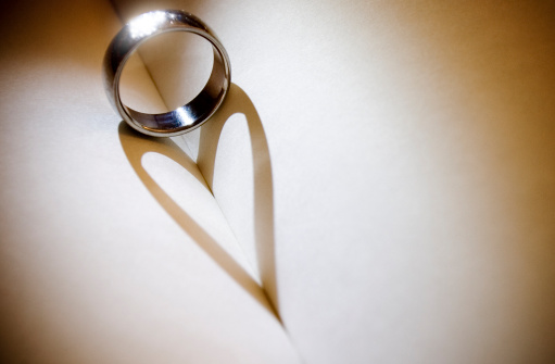 Wedding band casting shadow of a heart onto the pages of a register.