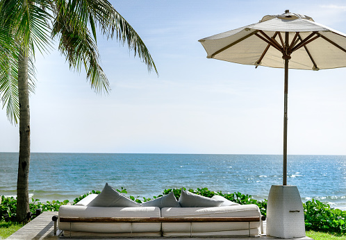 Sofa set overlooking the beach, sea, beach umbrellas, coconut trees and green grass. blue sky