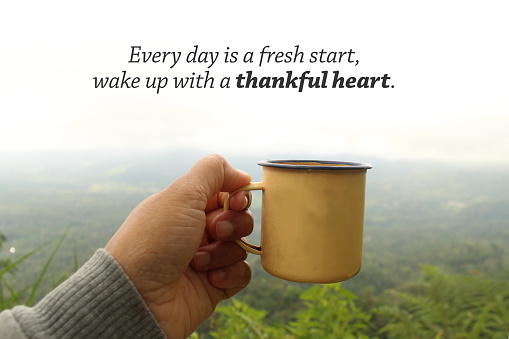 Grateful inspirational quote - Every day is a fresh start, wake up with a thank heart. Hand holding tea or coffee cup on foggy mountain background in a misty morning. Morning relax with tea outdoor.