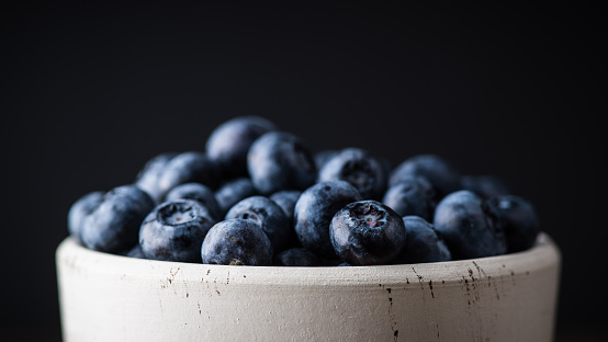 Blueberries in white ceramic bowl on rustic wooden background. Selective focus. Shallow depth of field.