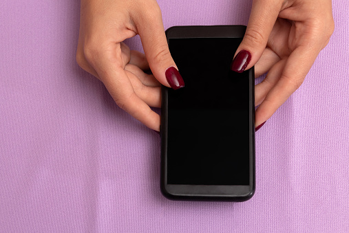 Female hands are holding black smartphone. Purple background with place for text. Advertising of gifts. Selective focus.
