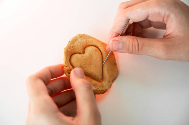 Hands closeup scratch brown sugar caramel candy cookies with a metal needle in the shape of a heart on a white backgound