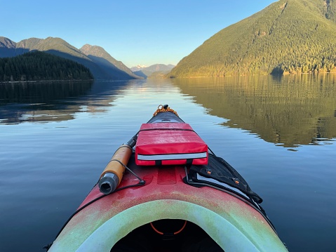 Kayaking on a calm lake surrounded by mountains, old growth forests and a clear blue sky