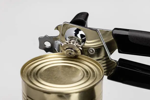 Photo of A can opener opening a can of food. Kitchen utensils, close-up.